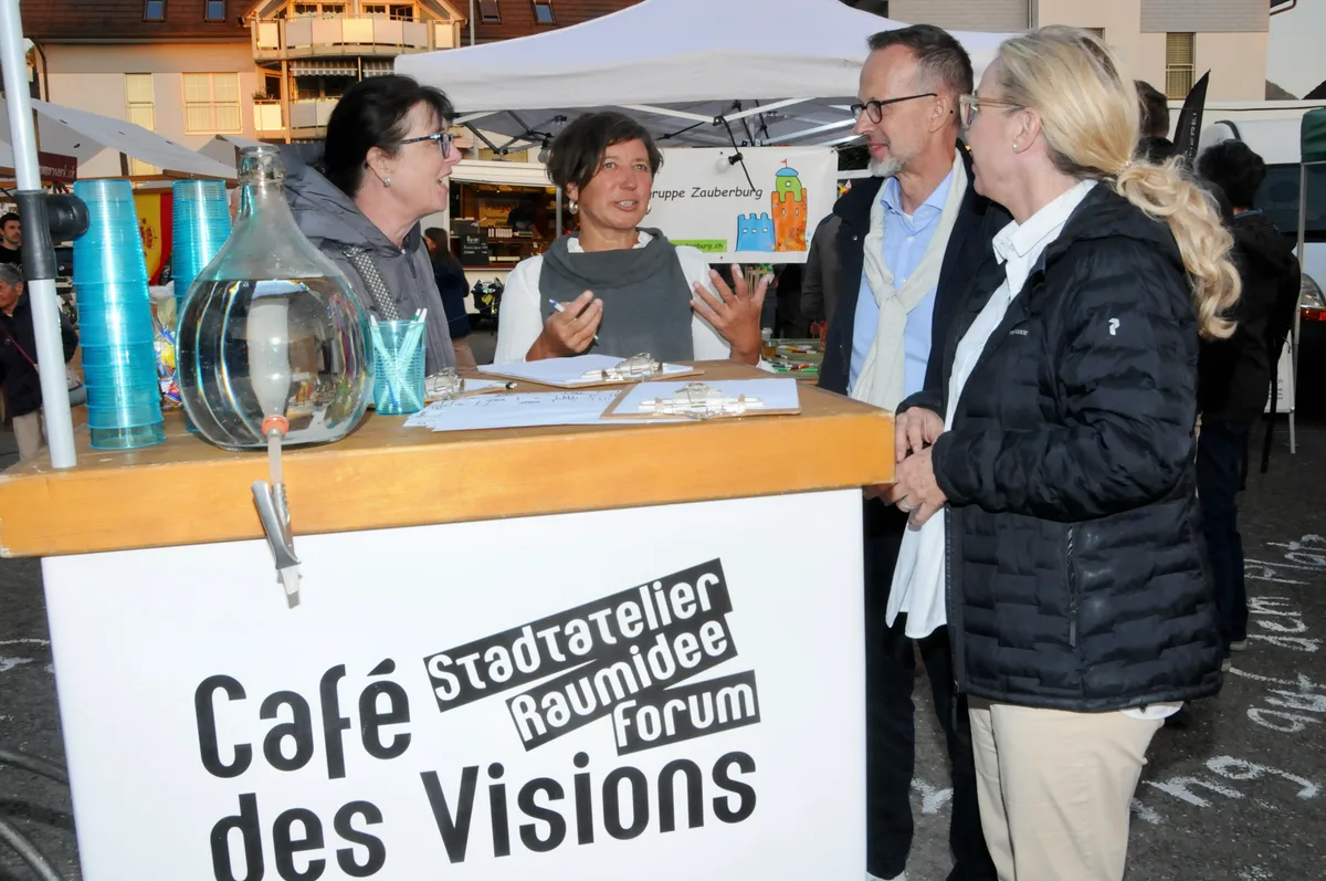 Man sieht vier Leute an einem Stand stehen.